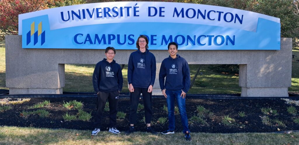 Enzo et d'autres étudiants de TSE devant le logo de l'Université de Moncton au Canada